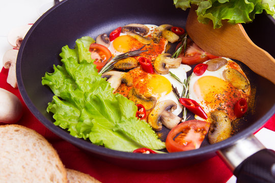 Homemade fried eggs in pan with tomato, bread, pepper, salad and mushrooms on the table