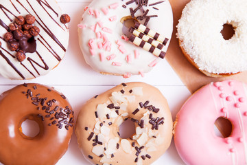 Six colored donuts with sprinkles and glaze on a white wooden background