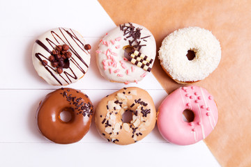 Six colored donuts with sprinkles on a white wooden background