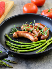 Fried sausages with asparagus, tomatoes and rosemary on a pan