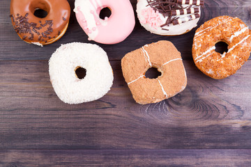 Colorful delicious donuts with chocolate, coconut and other sprinkles on a dark wooden background. Top view with copy space