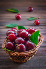 Cherries with leaves in a basket on wooden background