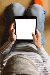 woman in striped sweater and jeans sitting on the floor in the room and works on the tablet. Top view