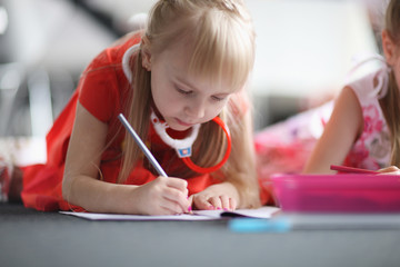 Portrait of a diligent schoolgirl drawing in her notebook while lying on the floor