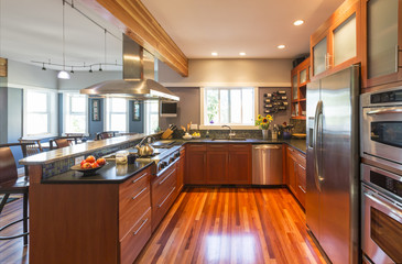 Spacious contemporary upscale home kitchen interior with wood cabinets & floors, accent lighting,...