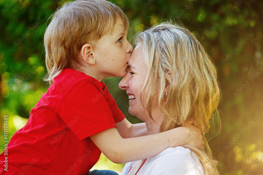 Wall mural happy little boy hugging and kissing his mother over green backg