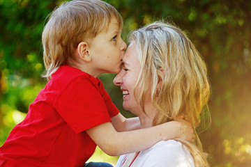 Happy little boy hugging and kissing his mother over green backg