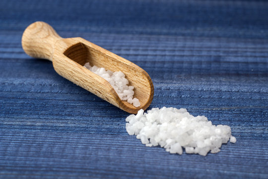 Salt crystals with wooden spoon on blue wooden background