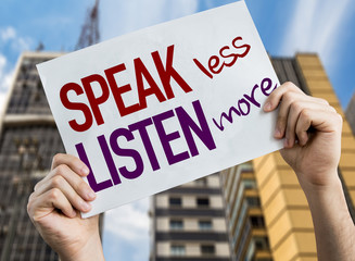 Speak Less Listen More placard with cityscape background