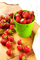 Fresh and ripe strawberries in a green metal bucket on a rustic wooden background