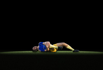 Professional young football to experience pain lying on grass - obrazy, fototapety, plakaty