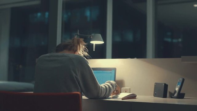 Young tired woman having headache and pain in the neck, using laptop computer at night or in the evening. Teenage girl or student studying or working till late. Overworking business woman.
