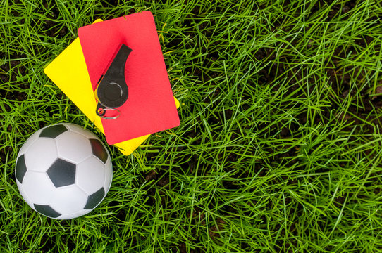 Soccer referee outfit a yellow and red card with ball on lawn of stadium. Football background