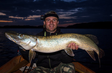 Happy angler with monster pike at evening time