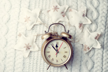 Image of alarm clock on knitted background sorounded with decorative stars
