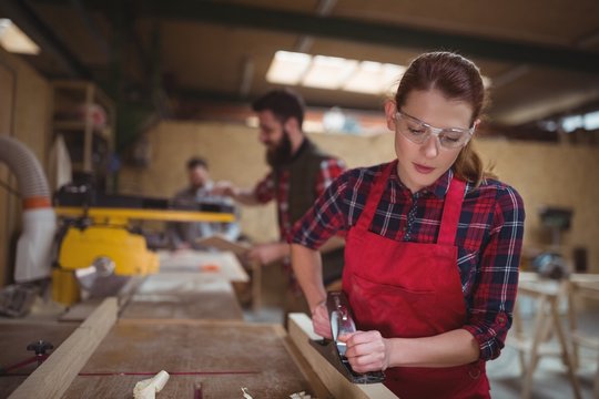 Female carpenter leveling a timber with jack plane