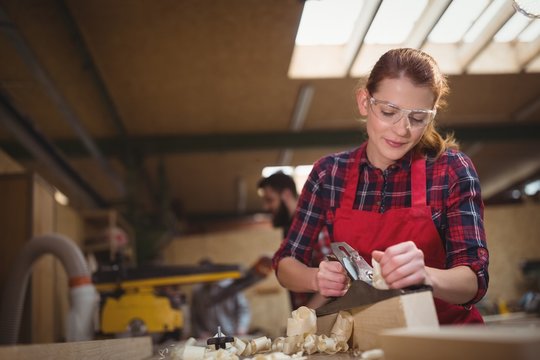 Female carpenter leveling a timber with jack plane