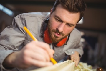 Carpenter marking on wooden plank with pencil