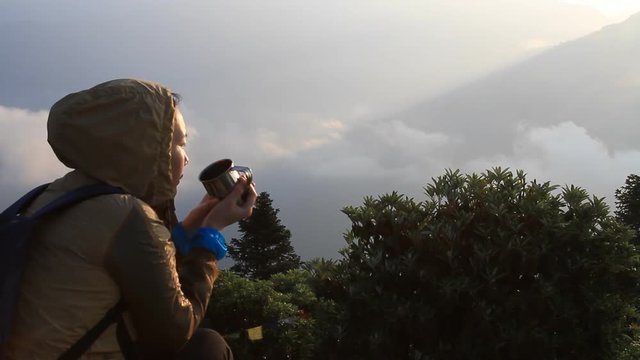 Asian woman watching the sunrise from the observatory of Poon Hill and drinking a cup of coffee in Nepal 