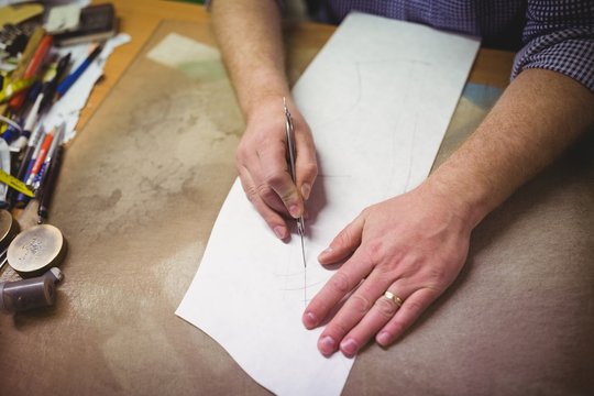 Cobbler cutting a design of shoe from paper