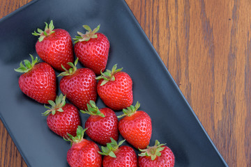Strawberries with stems on a black platter
