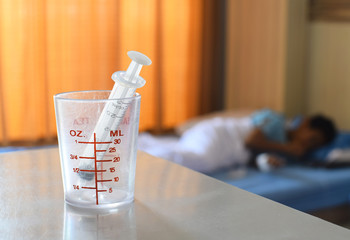Syringe in a dirty glass measuring cup with blurred patient in background