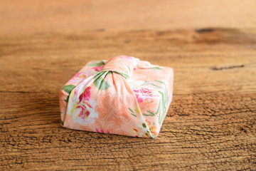 Gift box wrapped with Thai traditional style cloth tie on wood background