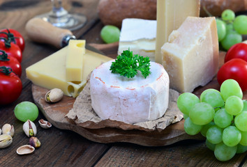 Käseplatte mit Brie, Parmesan, Emmentaler und Gruyere auf Holz mit Trauben und Kirschtomaten