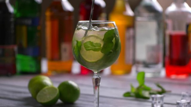 Green drink with ice. Spoon mixing cocktail in glass. Beverage with mint and lime. Tasty hugo cocktail with champagne.
