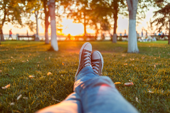 Male feet in gumshoes on green grass in the park at sunset