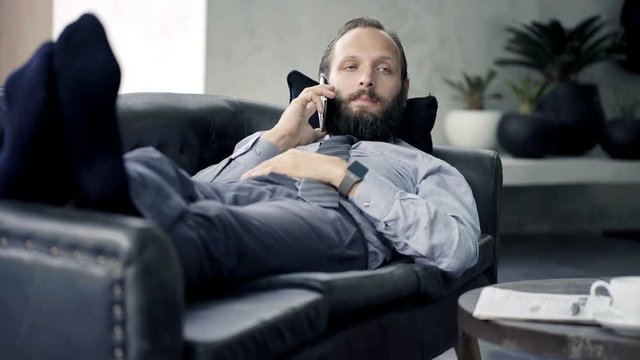 Young businessman talking on cellphone while lying on sofa at home
