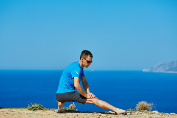 young man doing sports workout on the cliff against sea and blue sky at early morning