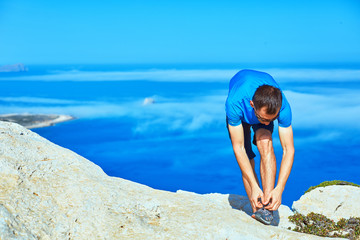 man runs on a rock against a blue sea. man leaned lace up sneakers