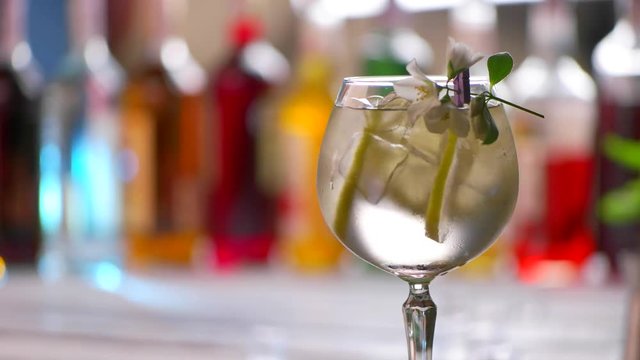 Glass of drink slowly rotates. Beverage with slices of lemon. Simple cocktail decorated with flower. Delicious tom collins at bar.