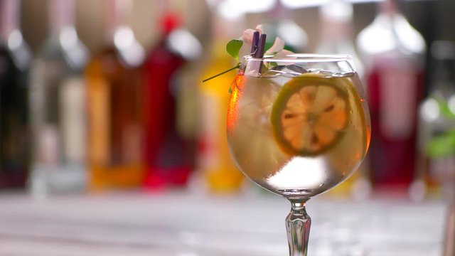 Flower on glass with cocktail. Glass of beverage rotates slowly. Tom collins decorated by flower. Feel the taste of summer.