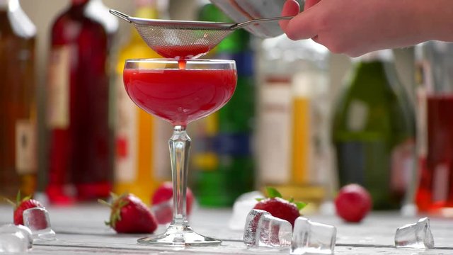 Red beverage in a glass. Hand holding sieve over glass. Fresh cocktail of strawberry. Preparation of clover club.