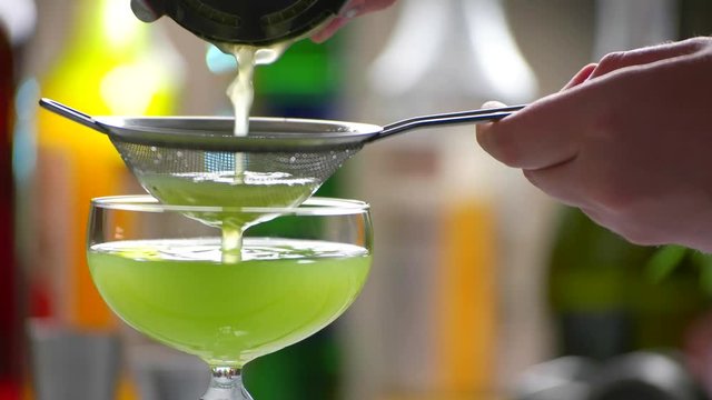 Green beverage pours through sieve. Hand holds sieve over drink. Delicious cocktail made by bartender. Kiwi daiquiri with fresh juice.
