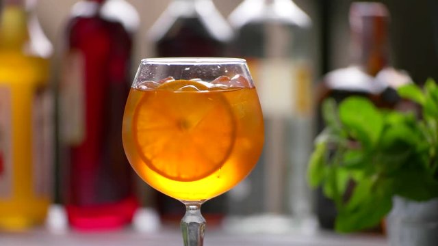 Tongs putting orange into cocktail. Slice of orange inside beverage. Delicious aperol spritz cocktail. Tasty drink with dry wine.