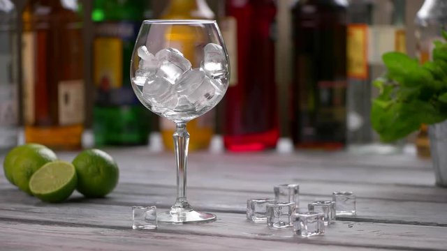 Ice cubes falling into glass. Limes beside a wineglass. Workplace of bartender in restaurant. Cubes of ice on table.