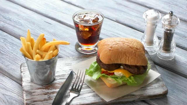 Dark drink pours into glass. Burger and french fries. Delicious food on bistro table. Original fresh burger with beef.