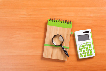 Plakat notebook on a brown wooden background with a calculator and magnifying glass
