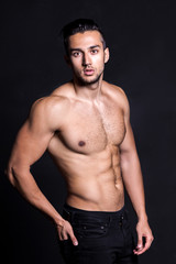 Sexy shirtless male model flirting against black background