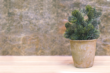 plastic tree in pot on wooden table and stone background, home d