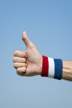 American athlete wearing USA colors red, white, and blue wristband holding thumbs up against blue sky