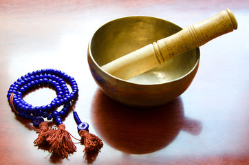 Closeup of a tibetan bowl and violet  mala beads for meditation on wooden background.