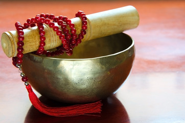Closeup of a tibetan bowl and red  mala beads for meditation on wooden background.