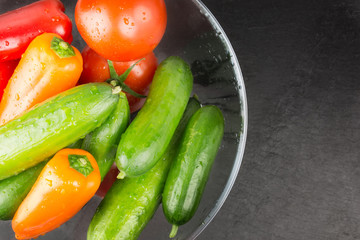 Washed organic vegetables in bowl on dark stone plate, top view
