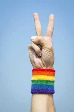 Gay athlete making peace sign with gay pride rainbow colors wristband against bright blue sky