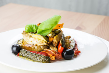 Roasted vegetables on a white plate on wooden background.