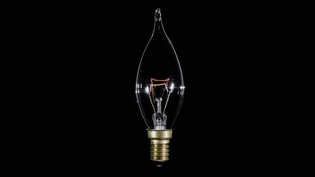 Candle shaped lamp light bulb flickers over black background, macro video, looped